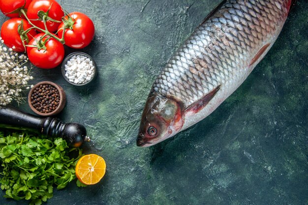 Vista superior de pescado crudo fresco con verduras y tomates sobre fondo oscuro
