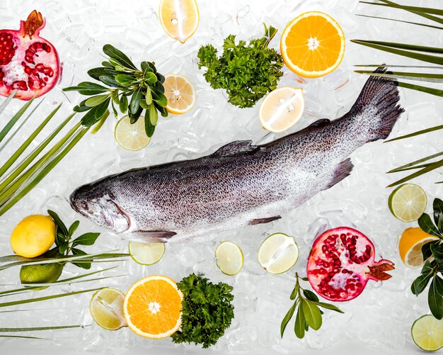 Vista superior de pescado crudo en hielo rodeado de frutas