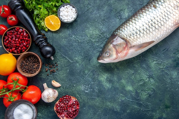 Vista superior de pescado crudo molinillo de pimienta tomates hojas de ajo granada diferentes especias en tazones pequeños en la mesa