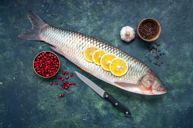 Vista superior de pescado crudo, pimienta negra, semillas de granada en tazones, cuchillo de ajo en la mesa