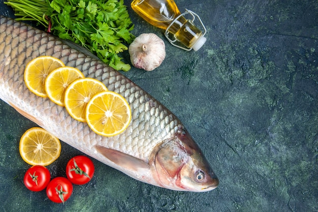 Vista superior de pescado crudo tomates rodajas de limón botella de aceite en el espacio libre de la mesa