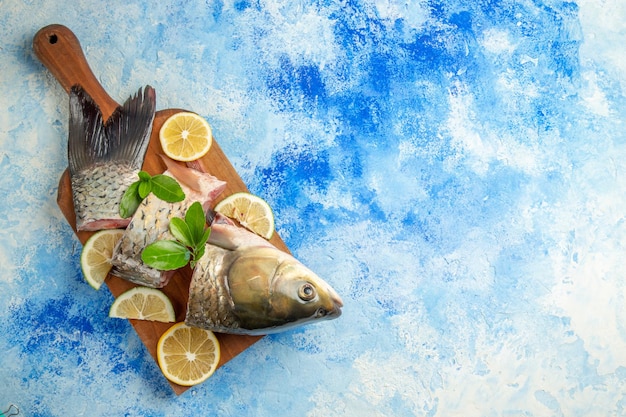 Vista superior de pescado fresco en rodajas con rodajas de limón sobre la superficie azul