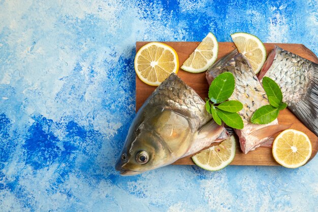 Vista superior de pescado fresco en rodajas con rodajas de limón sobre la superficie azul