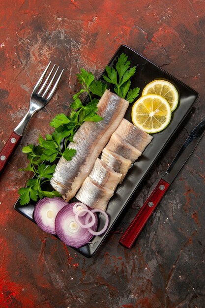 Vista superior de pescado fresco en rodajas con verduras y cebolla dentro de una sartén negra sobre el fondo oscuro