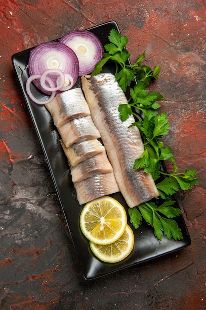 Vista superior de pescado fresco en rodajas con verduras y cebolla dentro de una sartén negra sobre el fondo oscuro