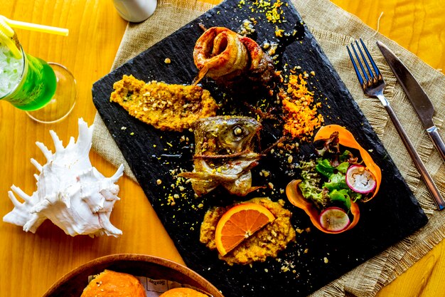 Vista superior de pescado frito enrollado con ensalada de verduras y decoración de rodaja de naranja