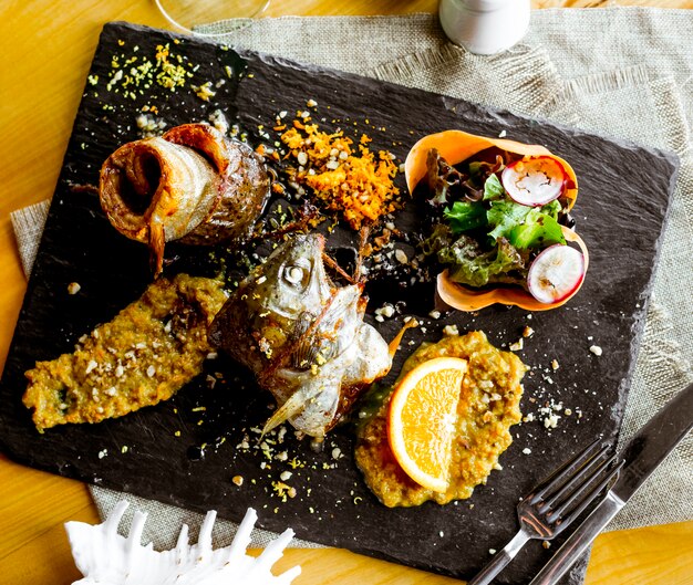 Vista superior pescado frito con salsa y una rodaja de naranja con verduras