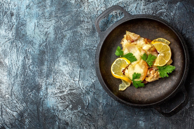 Vista superior de pescado frito en sartén con limón y perejil sobre fondo gris