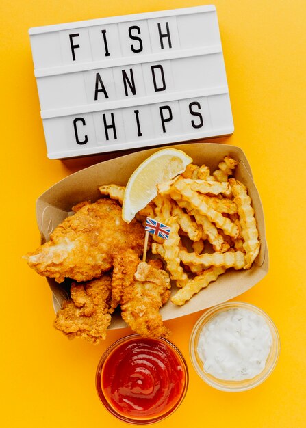 Vista superior de pescado y patatas fritas con caja de luz y salsa