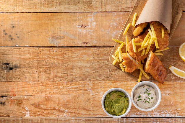 Foto gratuita vista superior de pescado y patatas fritas en cono de papel con espacio de copia y salsas