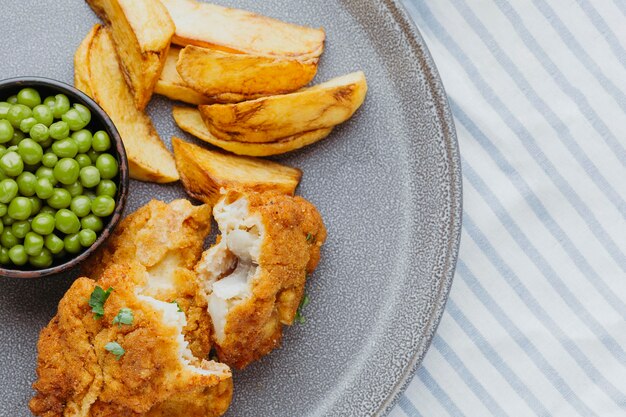 Vista superior de pescado y patatas fritas con guisantes en placa