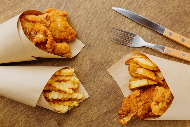 Vista superior de pescado y patatas fritas en papel con cubiertos