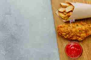 Foto gratuita vista superior de pescado y patatas fritas en papel con salsa de tomate y espacio de copia