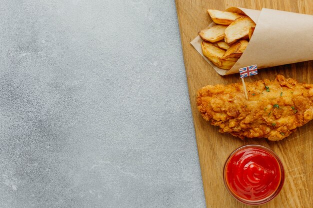 Vista superior de pescado y patatas fritas en papel con salsa de tomate y espacio de copia