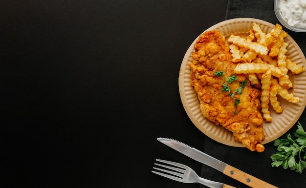 Foto gratuita vista superior de pescado y patatas fritas en un plato con cubiertos y espacio de copia