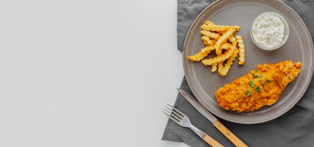 Vista superior de pescado y patatas fritas en un plato con espacio de copia