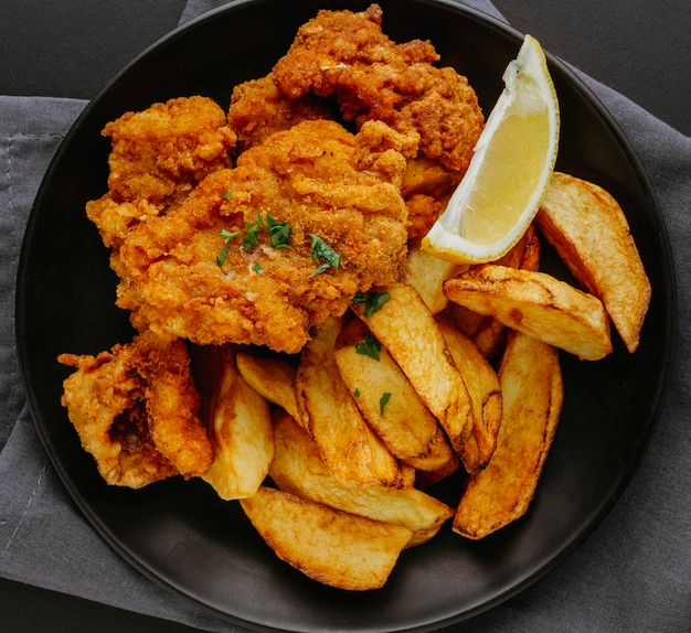 Vista superior de pescado y patatas fritas en un plato con una rodaja de limón