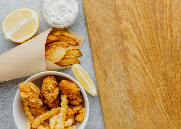 Vista superior de pescado y patatas fritas en un recipiente y envoltura de papel con espacio de copia y limón