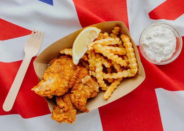 Vista superior de pescado y patatas fritas con rodaja de limón y bandera de gran bretaña