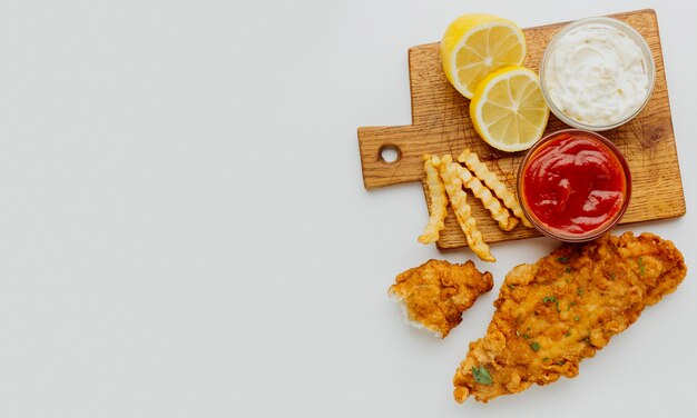 Vista superior de pescado y patatas fritas con salsa de tomate y espacio de copia