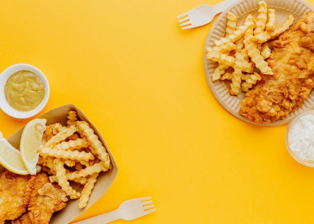 Vista superior de pescado y patatas fritas con salsas y tenedores