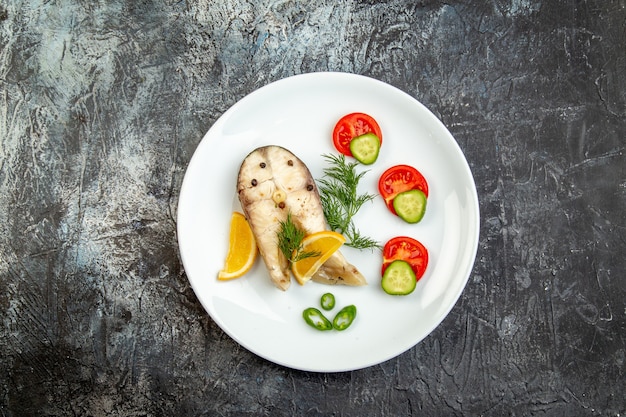 Vista superior de pescados crudos y alimentos frescos de pimienta en un plato blanco sobre la superficie del hielo gris