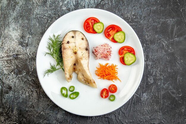 Vista superior de pescados crudos y alimentos frescos de pimienta en un plato blanco sobre la superficie del hielo