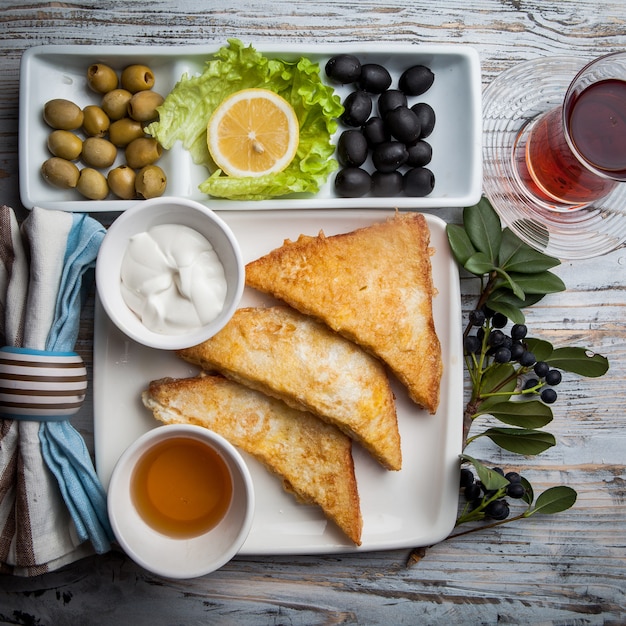 Vista superior de picatostes con una variedad de aceitunas y miel y un vaso de teaon plato blanco