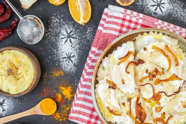 Vista superior de piezas de masa cocida con cebollas fritas y diferentes ingredientes en una superficie oscura