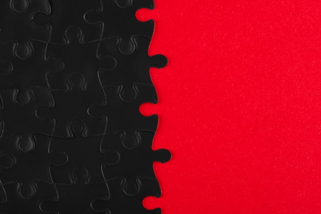 Vista superior de piezas de rompecabezas oscuras y fondo rojo.