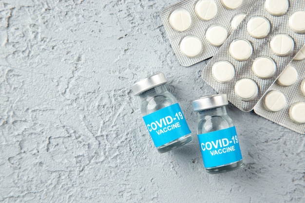 Foto gratuita vista superior de píldoras blancas empaquetadas y vacunas covid-en el lado izquierdo sobre fondo de arena gris con espacio libre