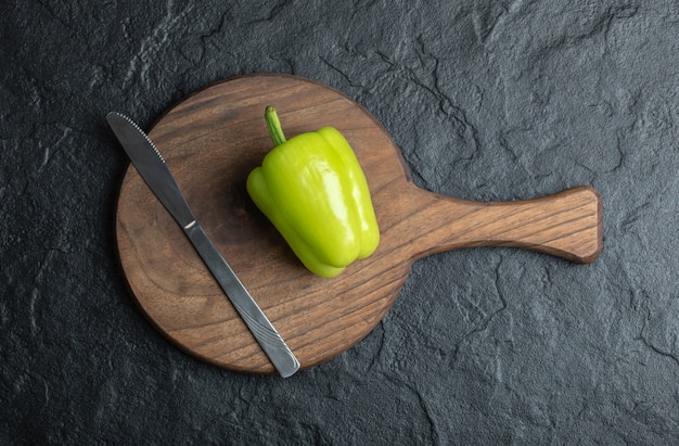 Vista superior de pimiento verde sobre una tabla de cortar de madera con un cuchillo.