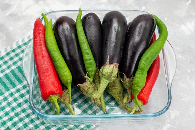 Vista superior de pimientos y berenjenas dentro de un recipiente de vidrio transparente en el escritorio brillante comida comida vegetal crudo