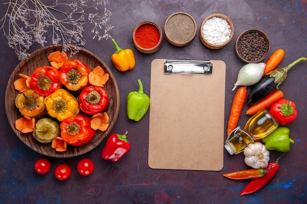 Vista superior de pimientos cocidos con verduras frescas y condimentos en la superficie gris oscuro, verduras dolma, carne de res