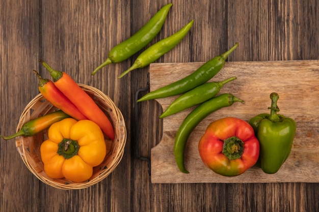 Vista superior de pimientos coloridos en una tabla de cocina de madera con pimientos amarillos y naranjas en un balde en una pared de madera