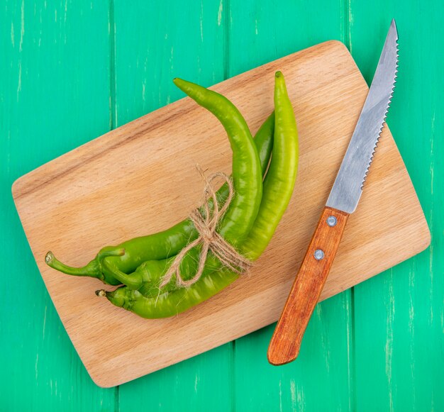 Vista superior de pimientos y cuchillo en tabla de cortar en superficie verde