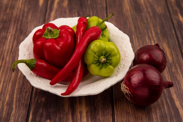 Vista superior de pimientos frescos y chiles en un recipiente con cebollas rojas aislado sobre un fondo de madera