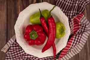 Foto gratuita vista superior de pimientos frescos y chiles en un recipiente sobre un paño marcado en una pared de madera