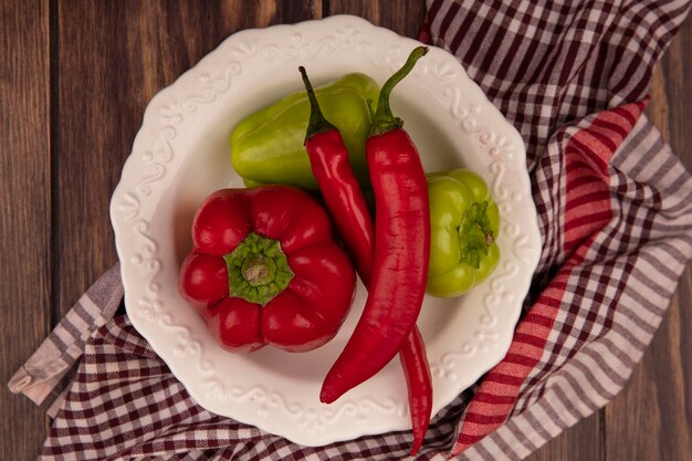 Vista superior de pimientos frescos y chiles en un recipiente sobre un paño marcado en una pared de madera