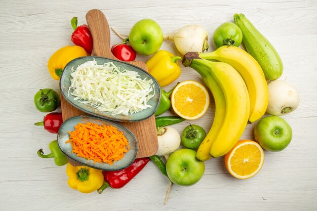 Vista superior de pimientos frescos con plátanos, manzanas y naranja sobre fondo blanco, ensalada, vida sana, foto, dieta de color maduro