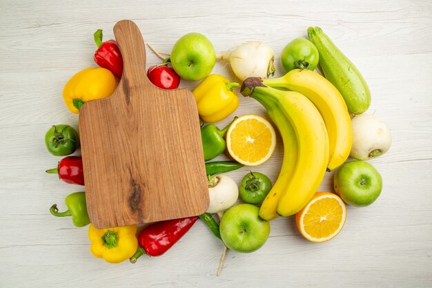 Vista superior de pimientos frescos con plátanos, manzanas y naranja sobre fondo blanco, ensalada, vida sana, foto, dieta de color maduro