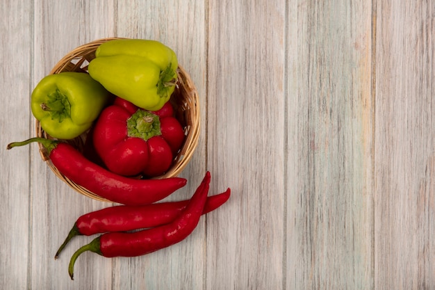 Vista superior de pimientos frescos y saludables en un balde con chiles aislado sobre un fondo de madera gris con espacio de copia