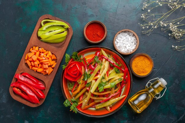 Vista superior de pimientos morrones en rodajas con ensalada de condimentos y aceite sobre fondo azul oscuro