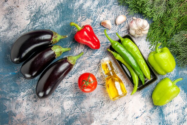 Vista superior de pimientos picantes verdes en un plato negro con ajo y pimientos rojos sobre fondo azul-blanco