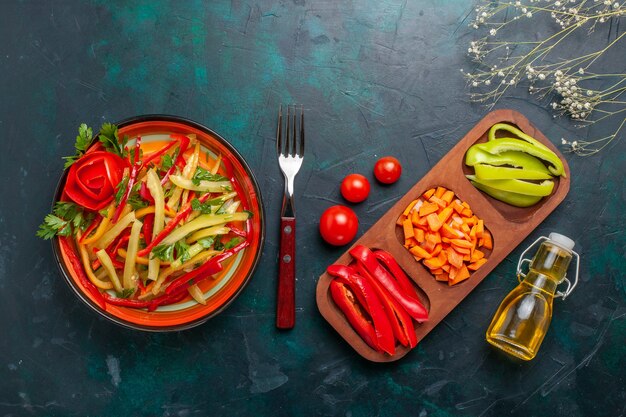 Vista superior de pimientos en rodajas ensalada de verduras de diferentes colores con ingredientes y aceite sobre fondo azul oscuro