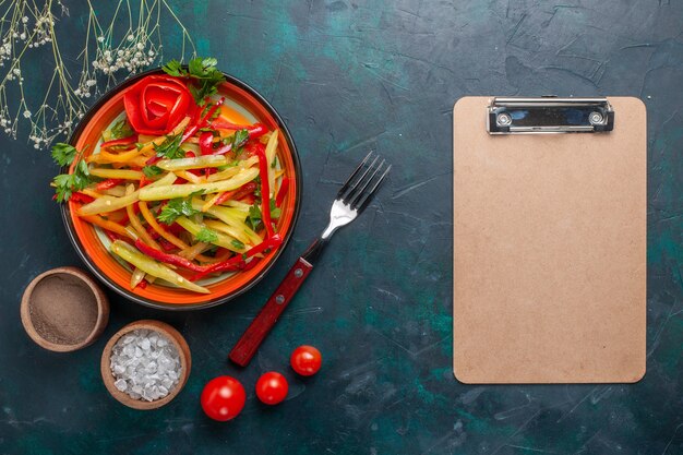 Vista superior de pimientos en rodajas sabrosa ensalada saludable con condimentos y bloc de notas sobre fondo oscuro