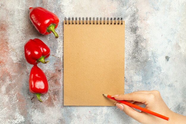 Vista superior de pimientos rojos un cuaderno lápiz rojo en la mano de la mujer en el espacio libre de la superficie desnuda