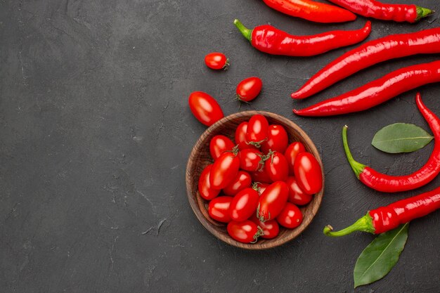 Vista superior de pimientos rojos y hojas de pago y un tazón de tomates cherry en el lado derecho de la mesa negra con espacio de copia