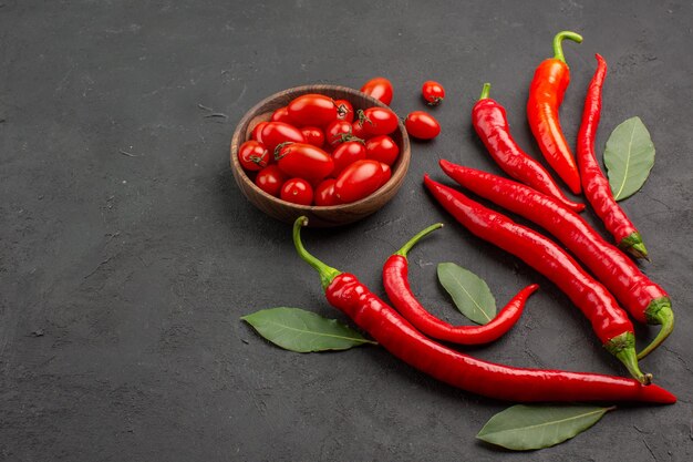 Vista superior de pimientos rojos y hojas de pago y un tazón de tomates cherry en una mesa negra con espacio libre