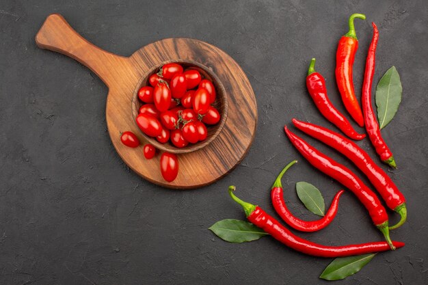 Vista superior de pimientos rojos y hojas de pago y un tazón de tomates cherry en la tabla de cortar sobre suelo negro con espacio libre